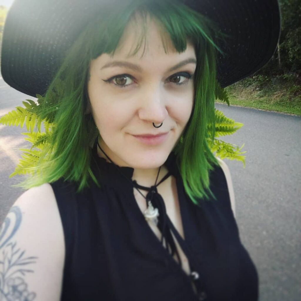A girl in black cut sleeves top matching hat posing for a selfie and showing her fern green hair color - green hair color