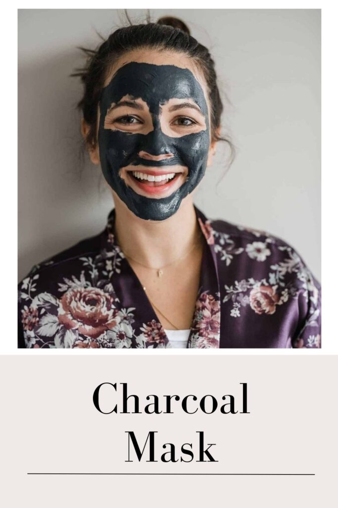 A smiling women in black floral dress on charcoal mask on her face - skin blemishes