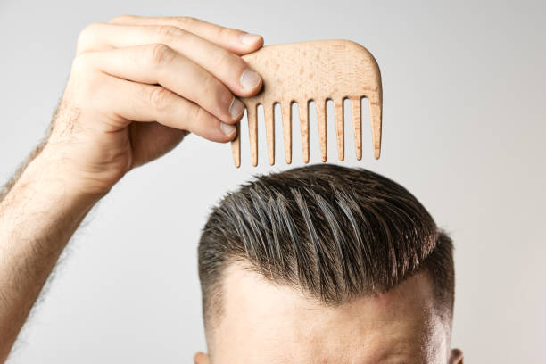 Man brushing his hair with a wooden comb and show how to take care about hair at home - comb curly hair men