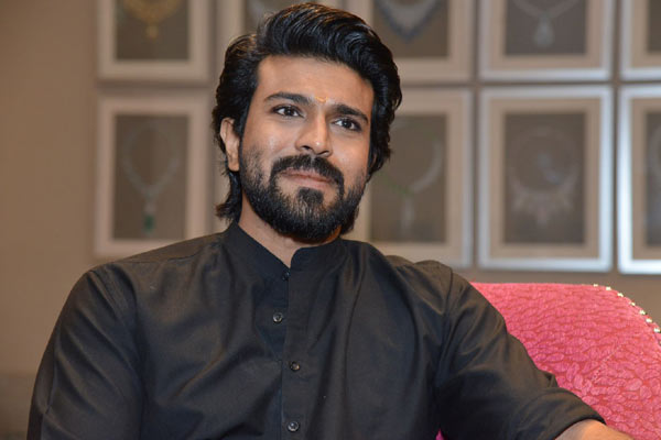 Ram Charan in black shirt sitting on a couch posing for camera - top 10 south indian actors 
