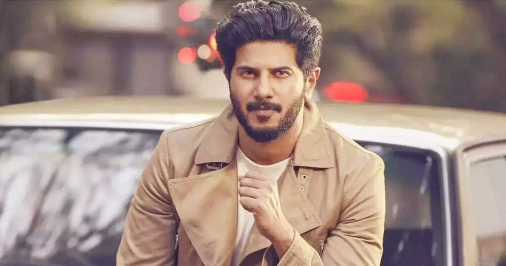 Dulquer Salman in beige color jacket with off white t-shirt sitting on a car and posing for camera - top 10 south indian actors 2022