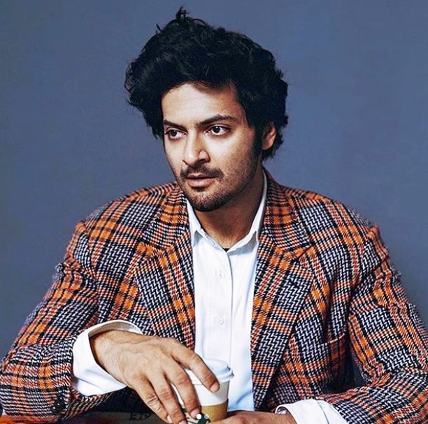 Ali Fazal in multi color coat with white shirt posing for camera and showing his side-swept retro hair look - bollywood actors hairstyles