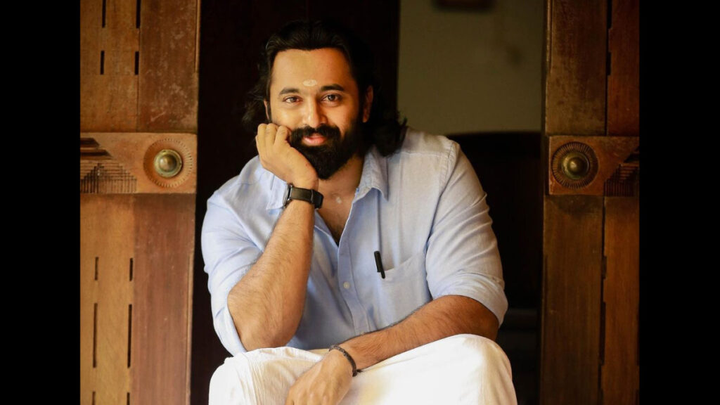Smiling Unni Mukundan in traditional south indian dress sitting and posing for camera - most googled south indian actors 2020