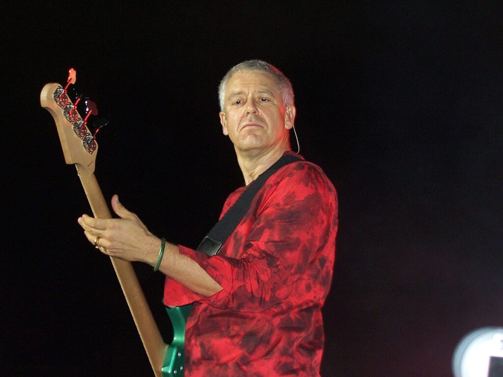 Adam Clayton in red and black shirt with guitar - Famous people with lasik