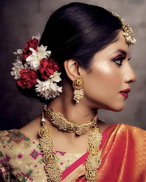 A girl in orange saree with multicolor blouse and heavy golden jewellery posing for camera and showing the side view of her Tight Bun Adorned with Artificial Flowers - hairstyles for Indian Wedding 