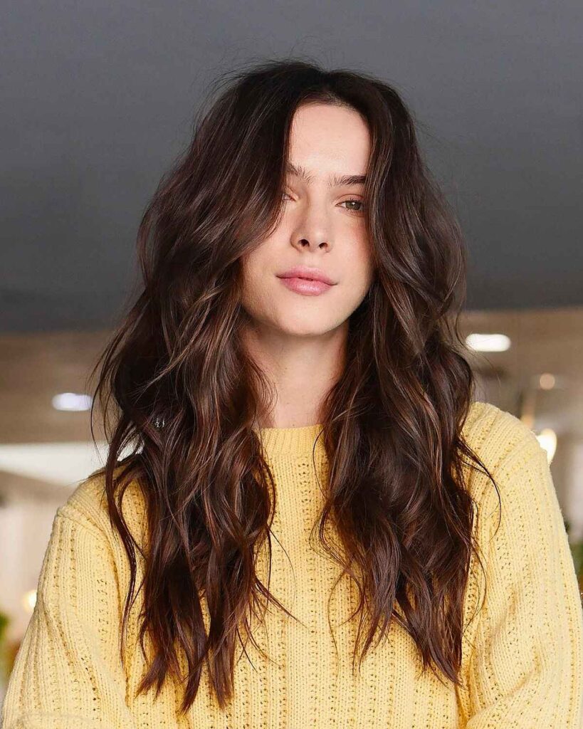 A women in yellow sweater posing for camera and showing her soft, wavy locks - Best American hairstyles