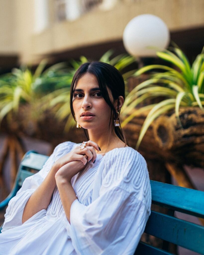 Aisha Ahmed in white dress sitting on a bench an posing for camera - beautiful indian girl instagram photos