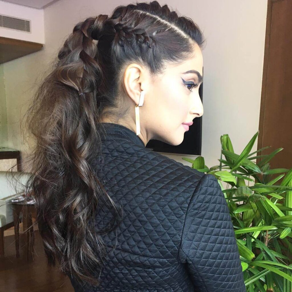 A women in black jacket and long golden earrings showing her braided ponytail - hairstyles for girls with curly hair
