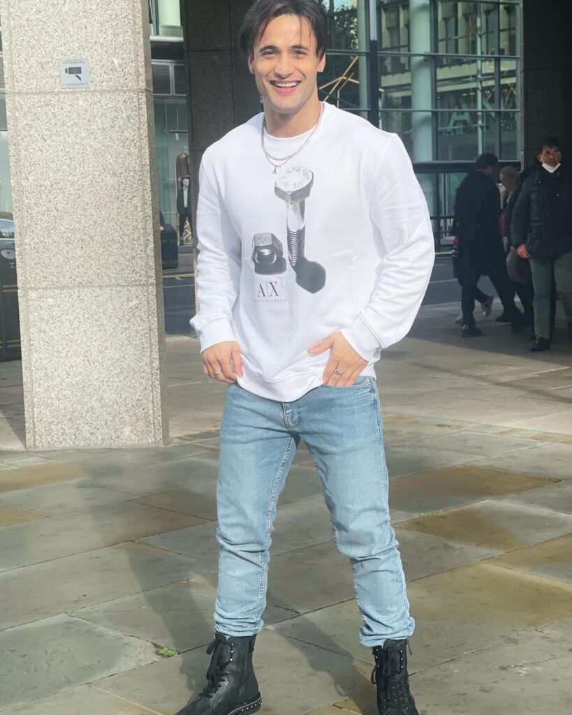 Smiling Asim Riaz in white full sleeves t-shirt with light blue jeans and boots posing for camera - most handsome tv actors indian