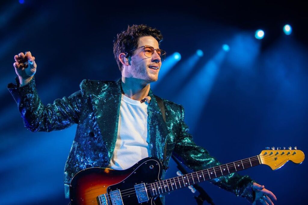 Nick Jonas in blue shimmery jacket with white t-shirt and goggles holding an guitar - indian celebrities with diabetes type 1