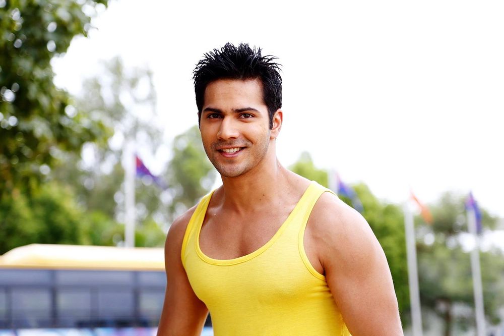 Smiling Varun Dhawan in yellow vest and showing his heavy voluminous hair with spikes - Varun Dhawan hairstyles