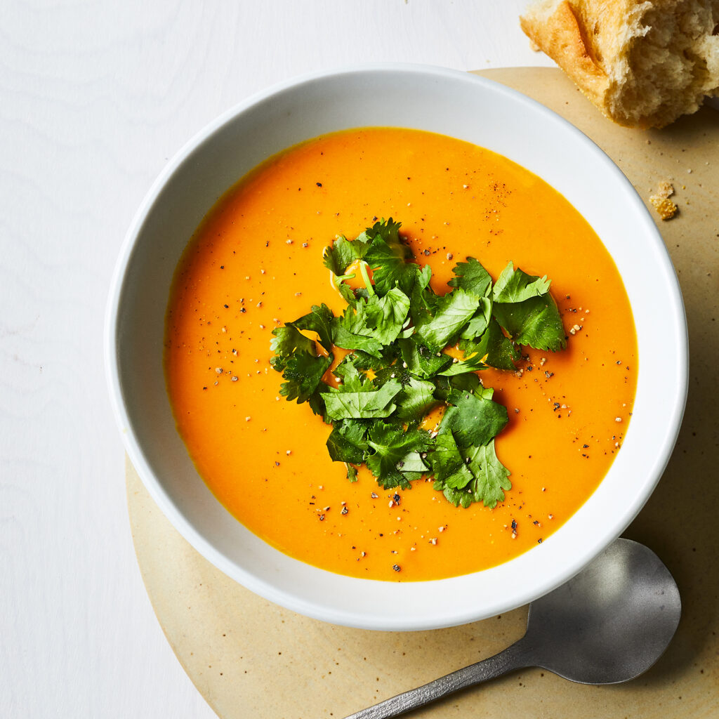 Spiced Carrot and Red Lentil Soup served in a white bowl garnished with fresh coriander leaves - Vegetarian fitness meal plan