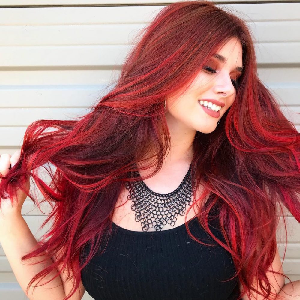 A smiling girl in black top with matching necklace showing her Vibrant Fire Engine Red hair color - hair color 2022