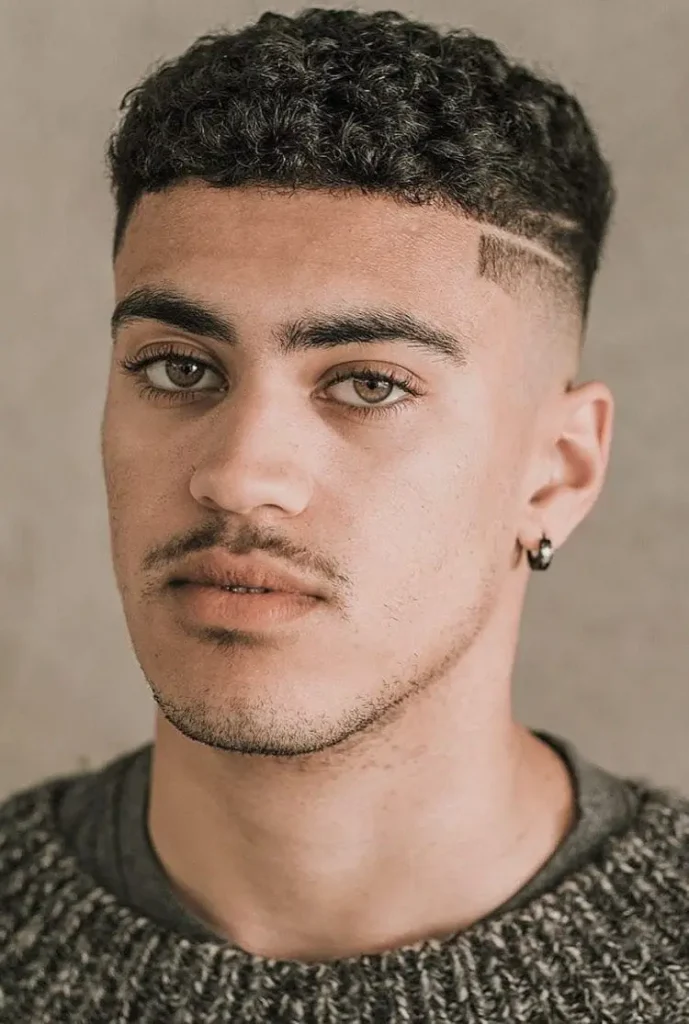 A man in grey pullover and a earring showing his Dense Short Curled Top with Shaved Lines hairstyle - haircuts for men