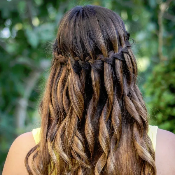 A girl in yellow cut sleeves top showing the back view of her waterfall braid - latest hairstyles for girls