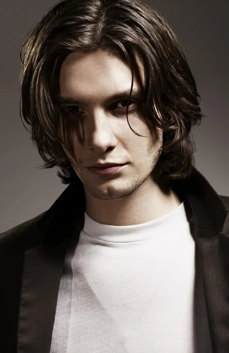 A man in black coat with white t-shirt showing his Middle Part hairstyle - long haircut for men