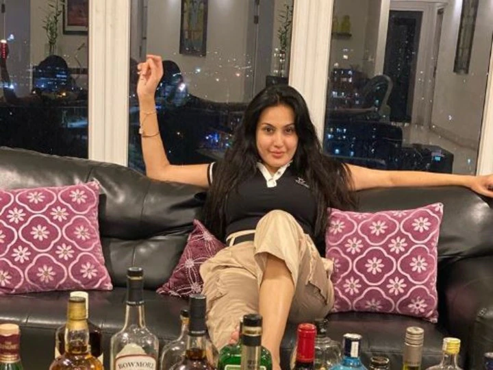 Kamya Punjabi in black t-shirt and beige half pants sitting on a sofa in front of a table full of whisky bottles - indian tv actress smoke