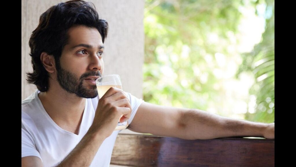 Varun Dhawan in white t-shirt sitting and drinking water - Varun Dhawan hair care routine