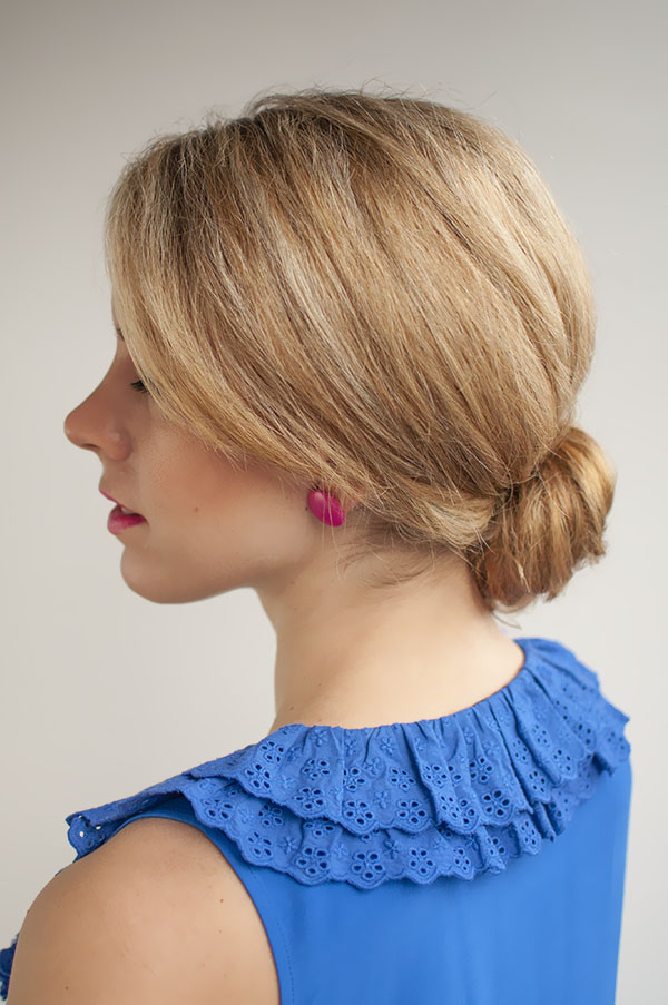 A woman in blue cut sleeves dress and pink stud earrings posing for camera and showing the side view of her Low Bun hairstyle - professional hairstyles for work