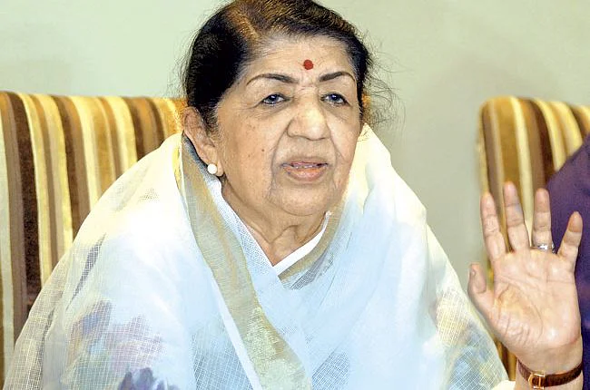 Lata Mangeshkar in white and golden saree sitting on a sofa - bollywood celebrities who passed away in 2022