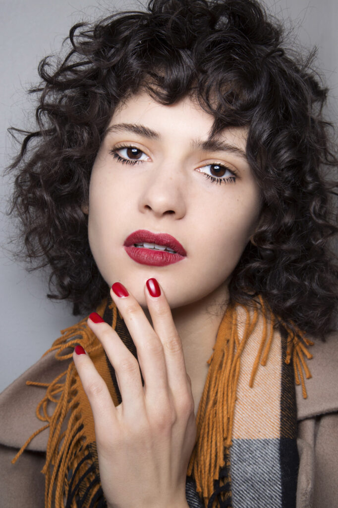 a girl in multicolor scarf with red lipstick and matching nail paint and Curly With Bangs hairstyle - daily hairstyles for medium hair